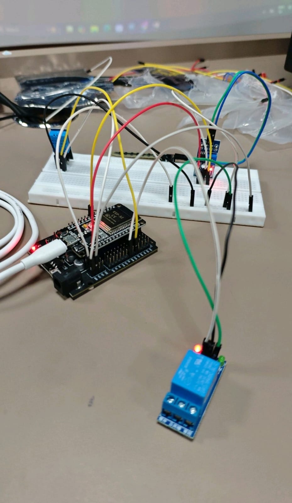 ESP32 board wired to a breadboard with glowing LEDs and a relay module on a workbench